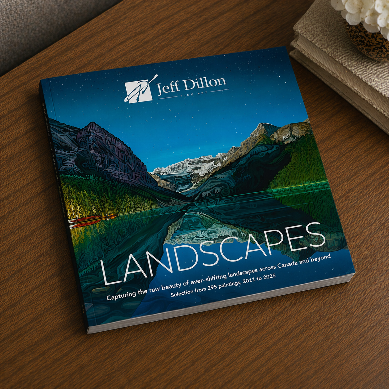 A close-up of the "Landscapes" Art Book by Jeff Dillon shows a Canadian mountain scene on the cover, with his logo and name at the top. The art book is slightly open, displaying its white pages inside.